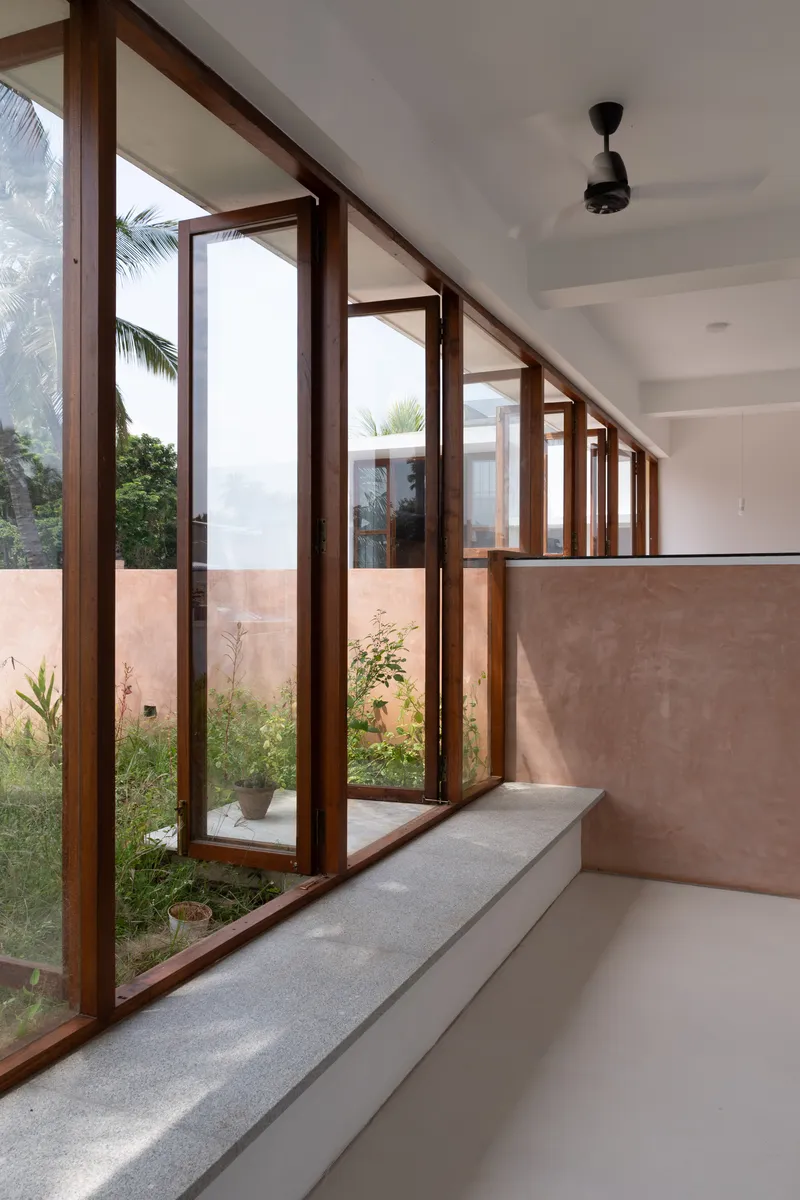 Row of timber-framed glazed doors with stepped sill overlooking planted courtyard under diffuse sky
