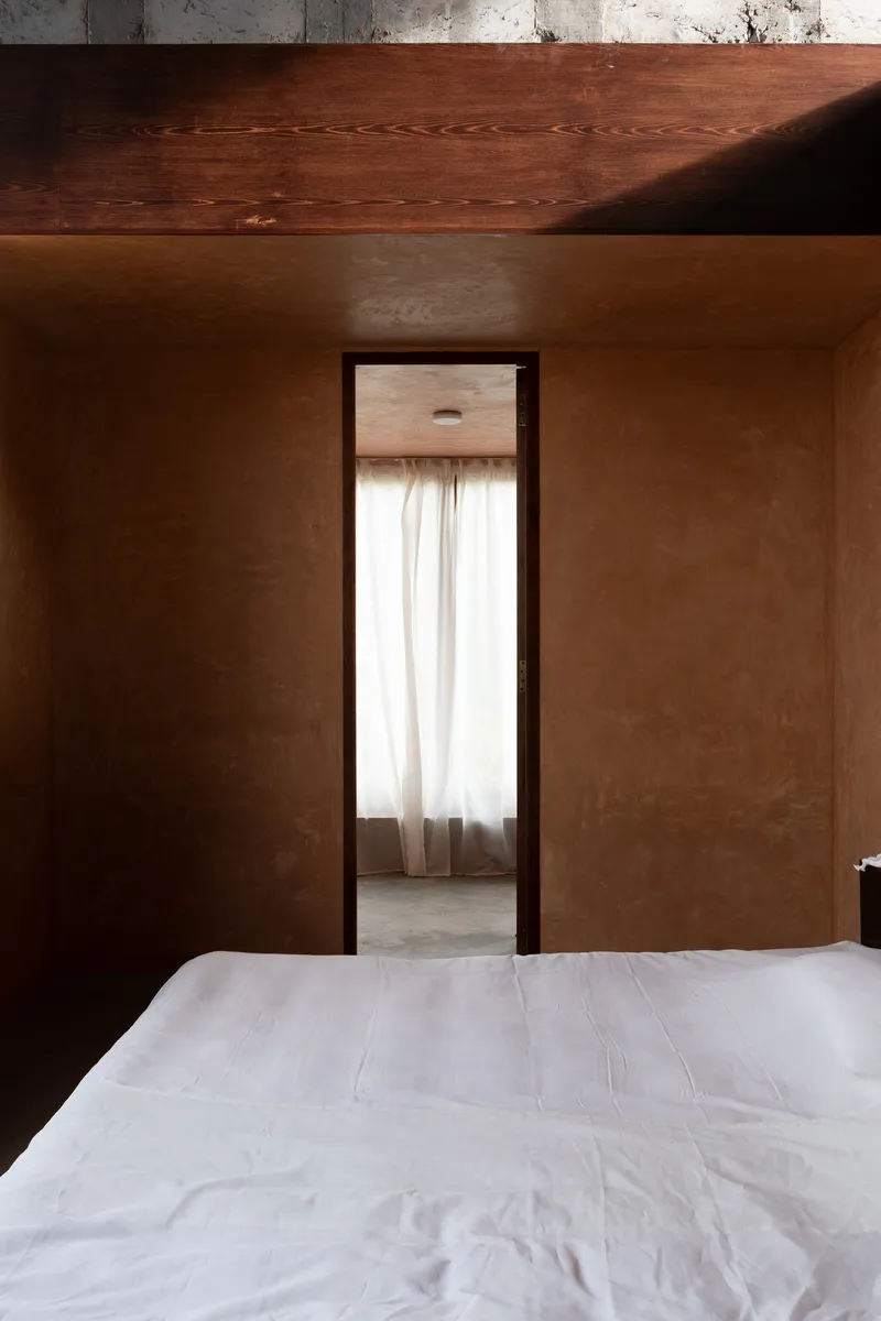 Bedroom doorway with pink plaster walls and timber-lined ceiling above a white bed