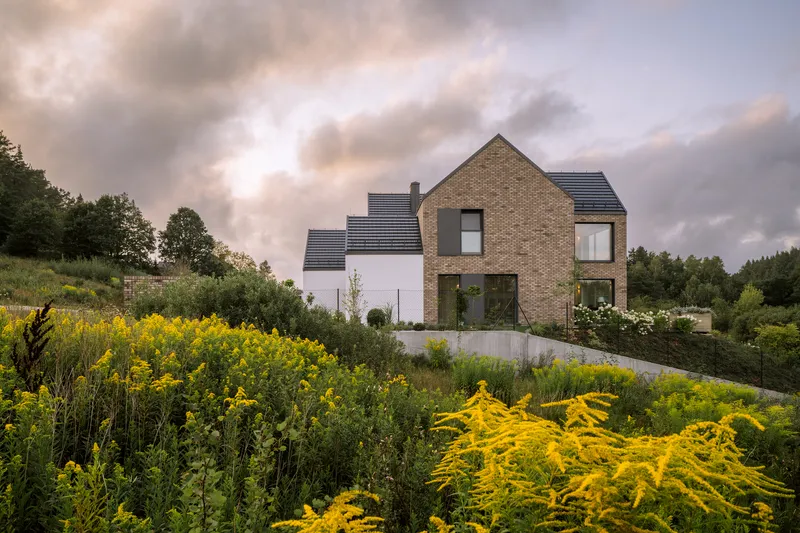 Brick and render gable facade rising above a garden of yellow flowering perennials under overcast skies