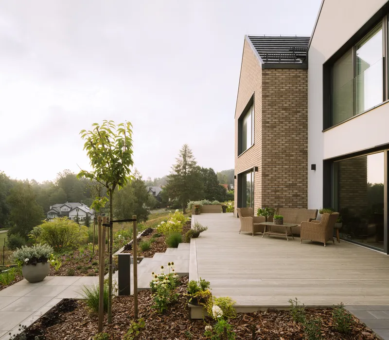Timber deck terrace with planted beds and wicker furniture adjoining brick and white rendered volumes