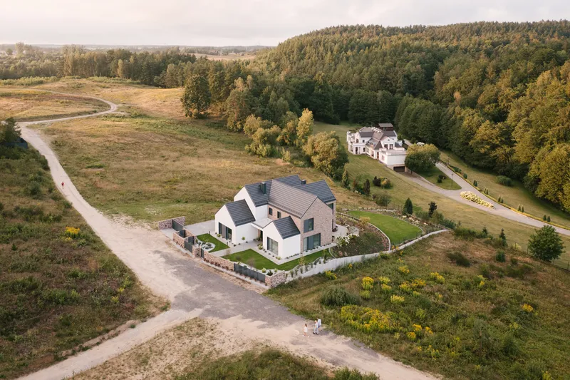 Aerial view of the gabled residence with terraced gardens surrounded by fields and forest