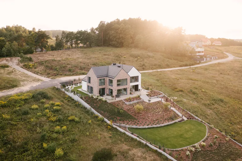 Drone view at sunset showing the house and curved garden beds within open farmland