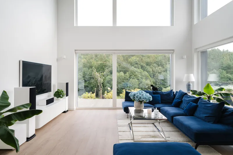 Double-height living room with sliding doors opening to trees and light wood flooring