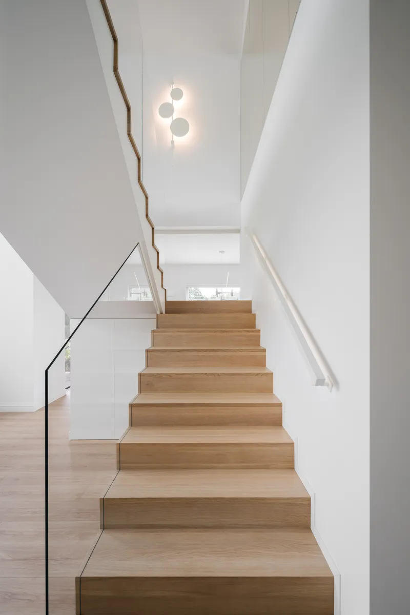 Light timber staircase with thin steel handrail and white walls beneath a circular pendant fixture