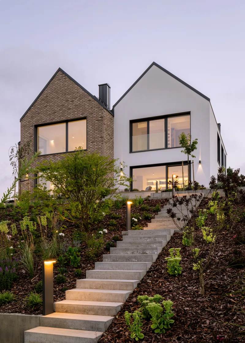 Two gabled volumes in white render and tan brick with landscaped steps at dusk