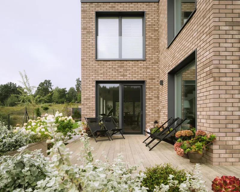 Timber deck terrace with lounge chairs set against the pale brick facade and white hydrangeas in bloom