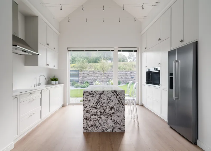 White galley kitchen with granite island, track lighting, and glass doors opening to the lawn beyond