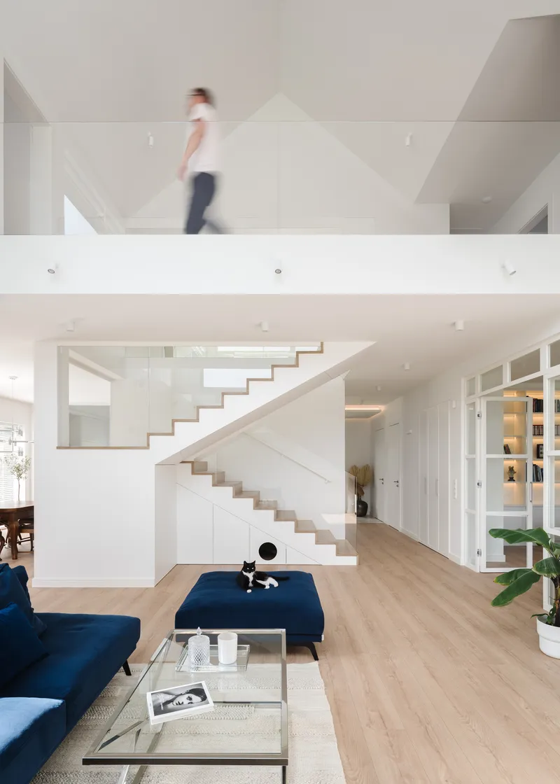 White floating staircase ascending through a double-height living room with a figure crossing the upper landing