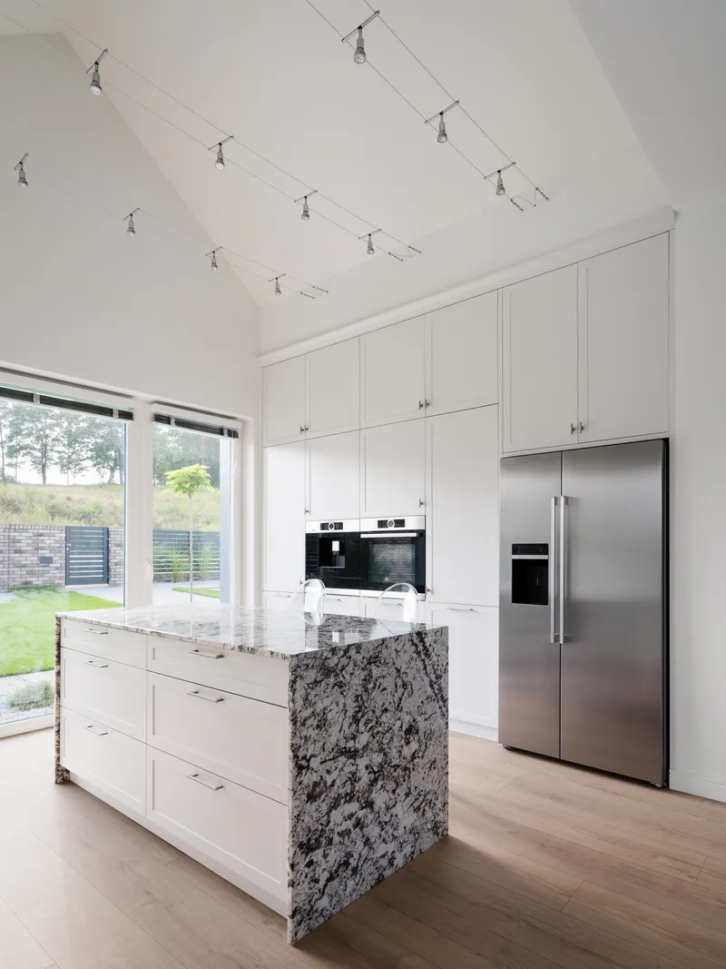 White kitchen with veined stone island and stainless appliances under track lighting