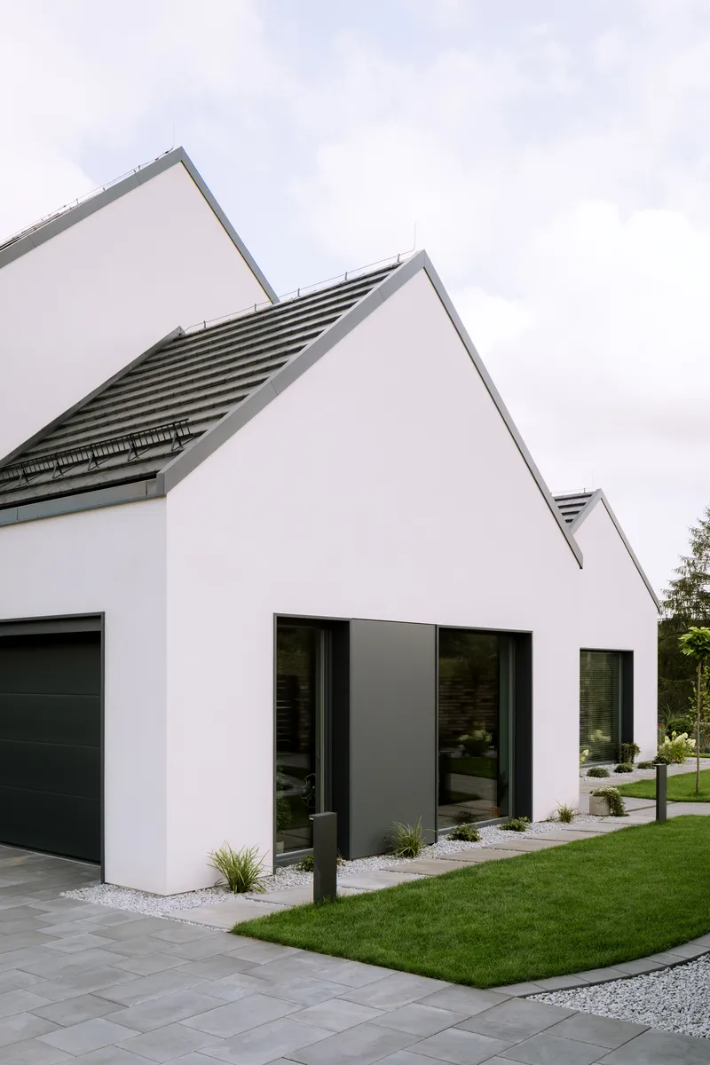 White gabled volumes with horizontal louver vents and large black-framed windows under overcast sky