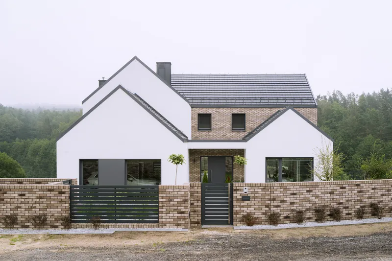 Front facade combining white stucco gables and brick upper story behind low variegated brick garden wall