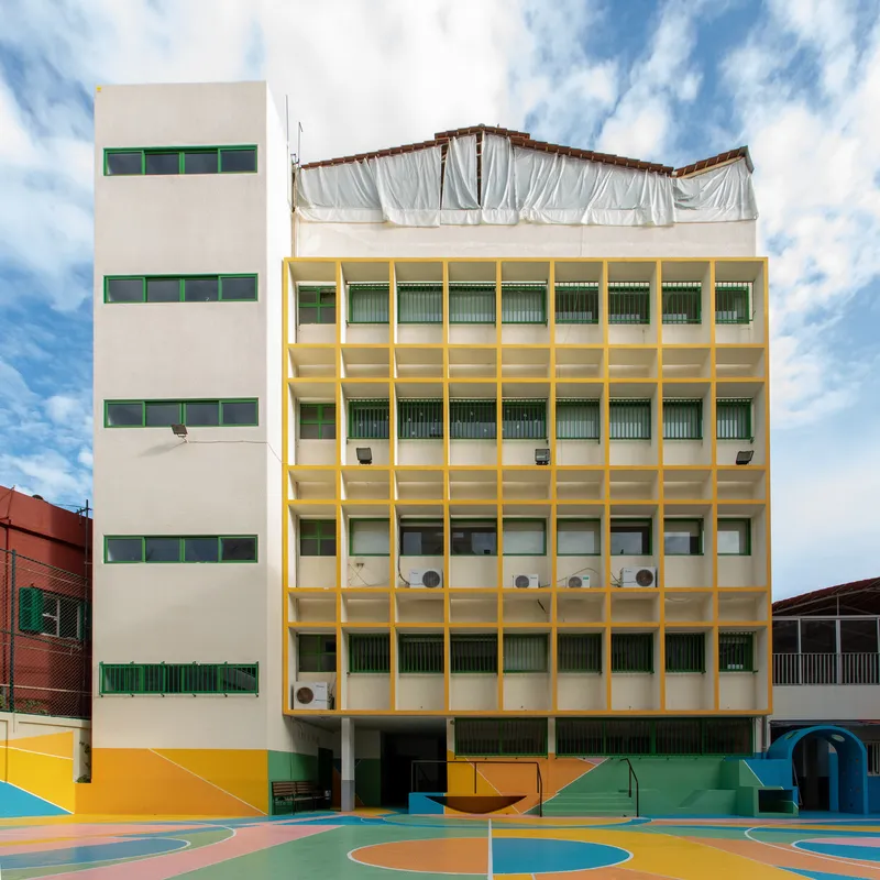 Yellow-framed classroom block with horizontal windows and white fabric screening the rooftop