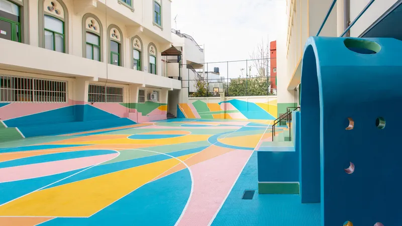 Multicolored basketball court with geometric paving pattern and blue climbing structure in a school courtyard