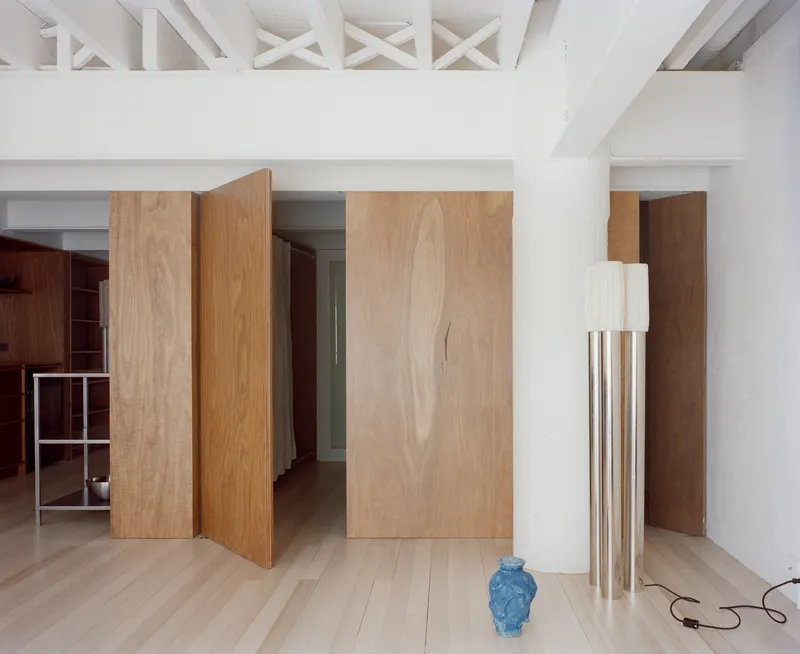Interior with pivoting wood veneer panels and exposed white-painted roof trusses above pale timber flooring