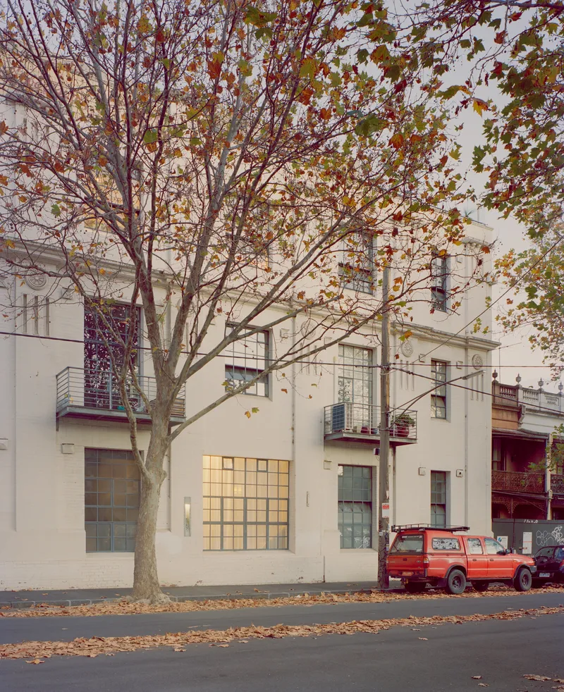 Street view of white rendered facade with grid block windows behind a bare deciduous tree in autumn