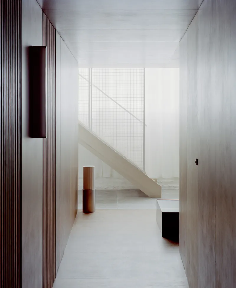Narrow hallway with fluted timber wall panels and pale stone staircase rising beneath a wire mesh screen