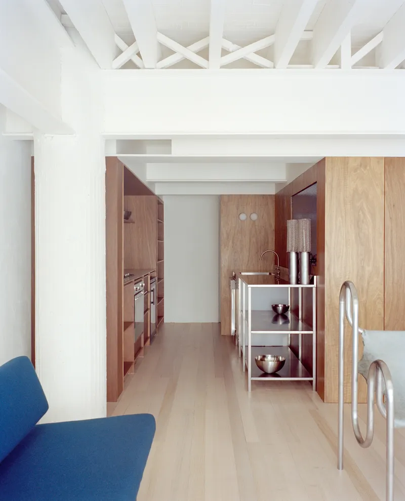 View into the galley kitchen showing wood cabinetry and a white metal trolley under exposed ceiling beams