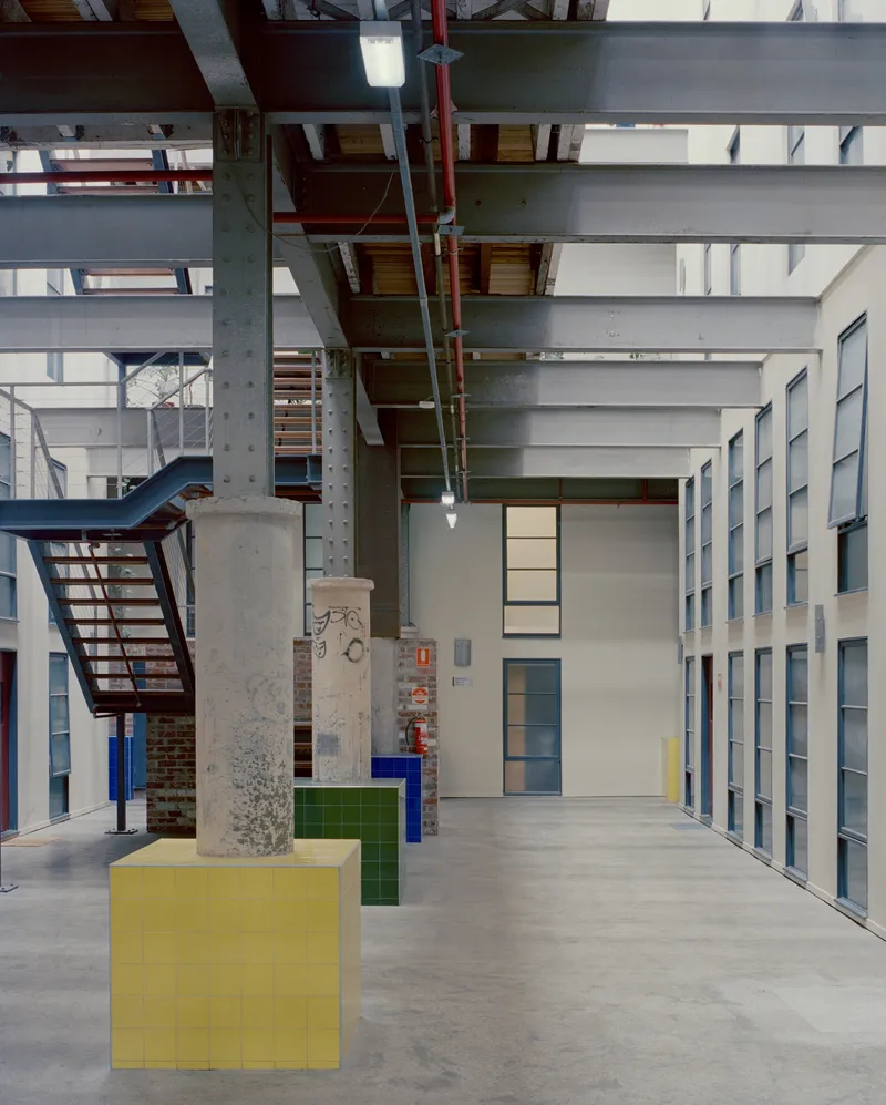 Interior hall with exposed steel beams, concrete columns, storage lockers and yellow and green plinth objects