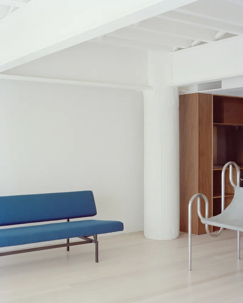 White room with exposed timber ceiling joists, blue upholstered sofa and cylindrical painted column