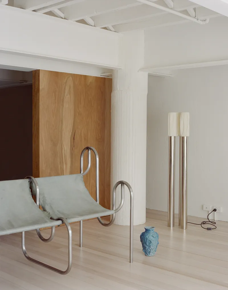 Interior with oak sliding panel, white column, tubular metal lounge chair and standing lamps