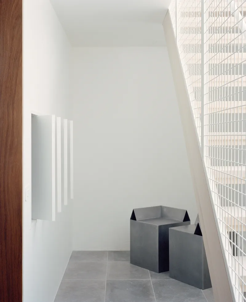Alcove with angled white walls, grey tile floor, metal bench sculpture and ribbed glass screen