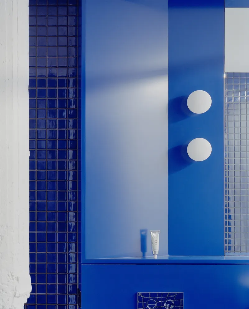 Blue tiled bathroom wall with white plaster surfaces and two circular sconces above a ledge