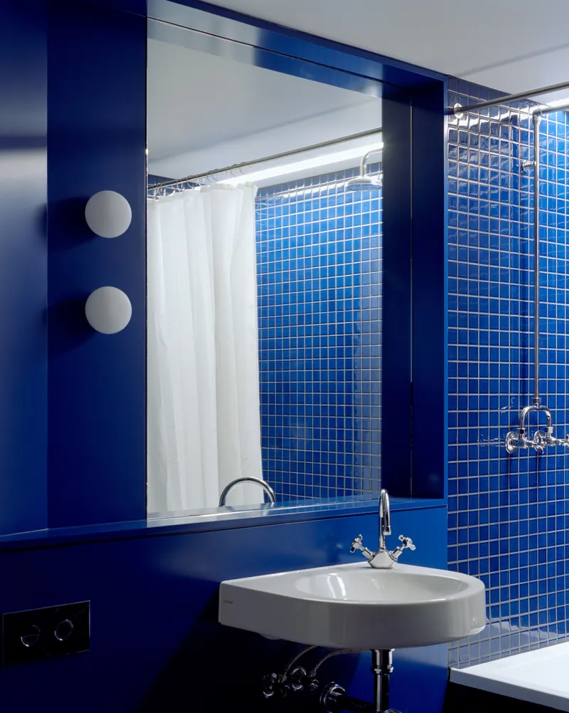 Bathroom mirror reflecting blue mosaic tile wall and white shower curtain with dual sconces