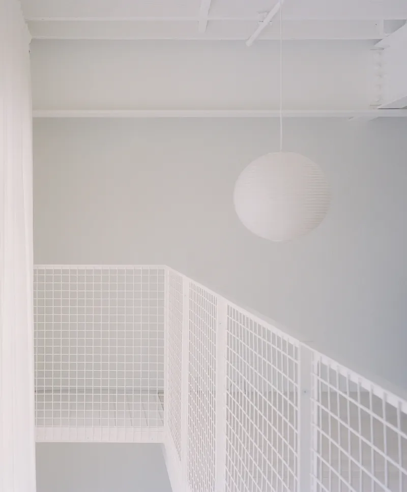 Upper level passage with white wire mesh railing and spherical pendant light under exposed joists