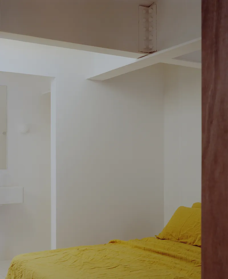 Bedroom corner with yellow bedding beside timber post and white wall partition