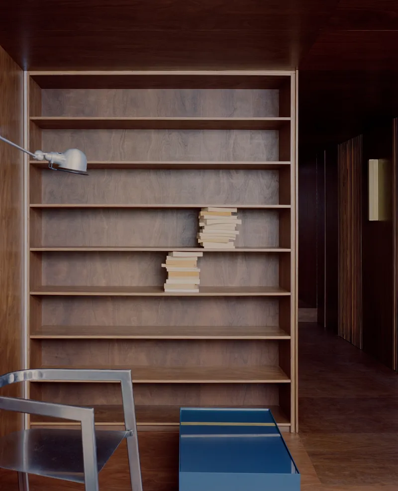 Built-in timber shelving unit with stacked books beside a dark hallway and blue storage box