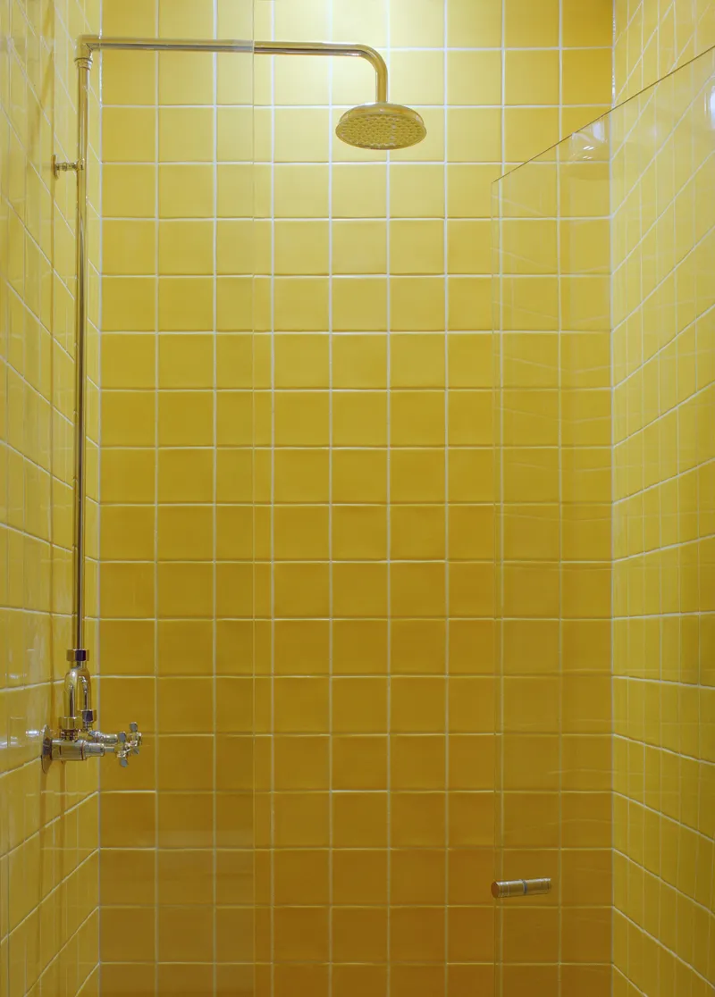 Yellow square-tiled shower enclosure with brass rain head and exposed plumbing fixtures