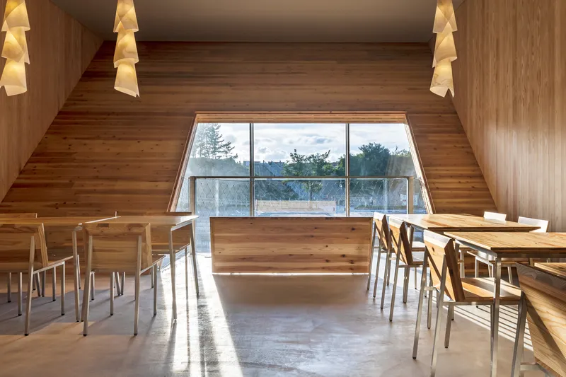 Interior dining space with timber walls, angled glazing, and pendant lights above tables and chairs