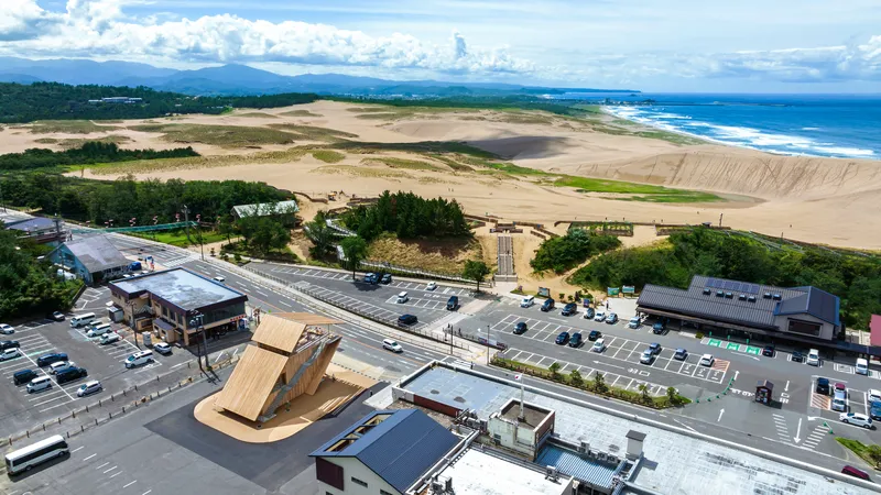 Aerial view of the timber pavilion in a parking lot beside coastal dunes and ocean waves