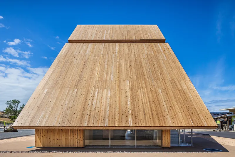 Frontal view of the inverted timber pyramid facade with horizontal slat cladding under clear blue sky