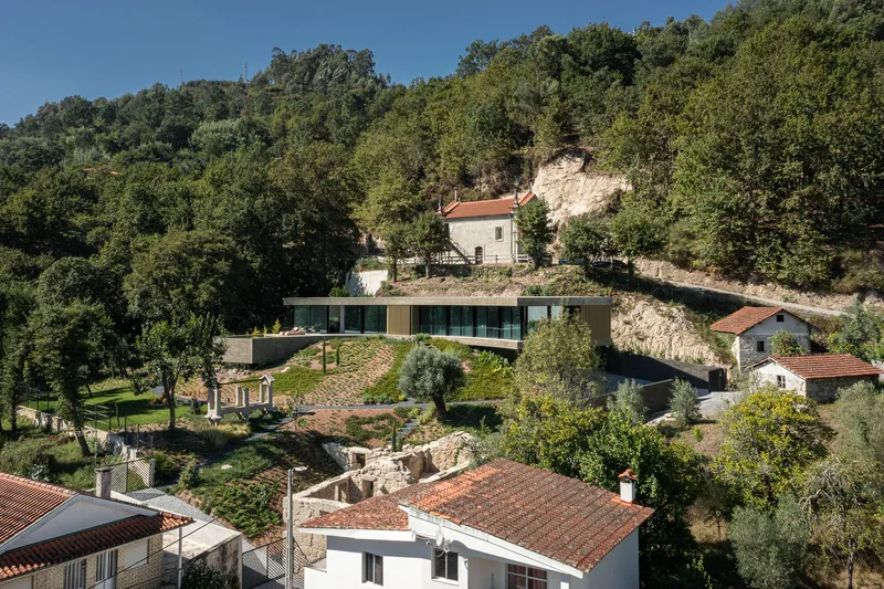 Hillside residence with horizontal glazed facade stepping down the terraced landscape among traditional tile-roofed houses