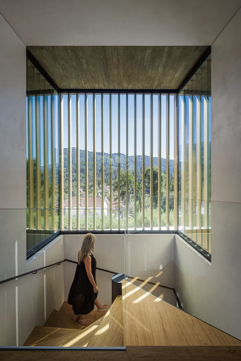 Stairwell with vertical timber sunscreen framing distant hills and casting striped shadows on the blonde timber treads
