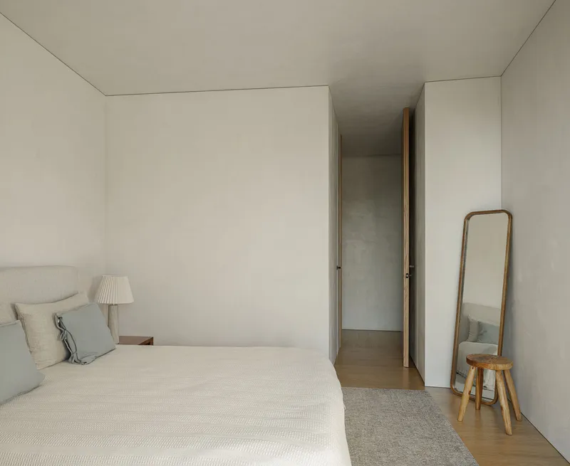 Bedroom with pale plaster walls and a narrow doorway leading to an adjacent corridor