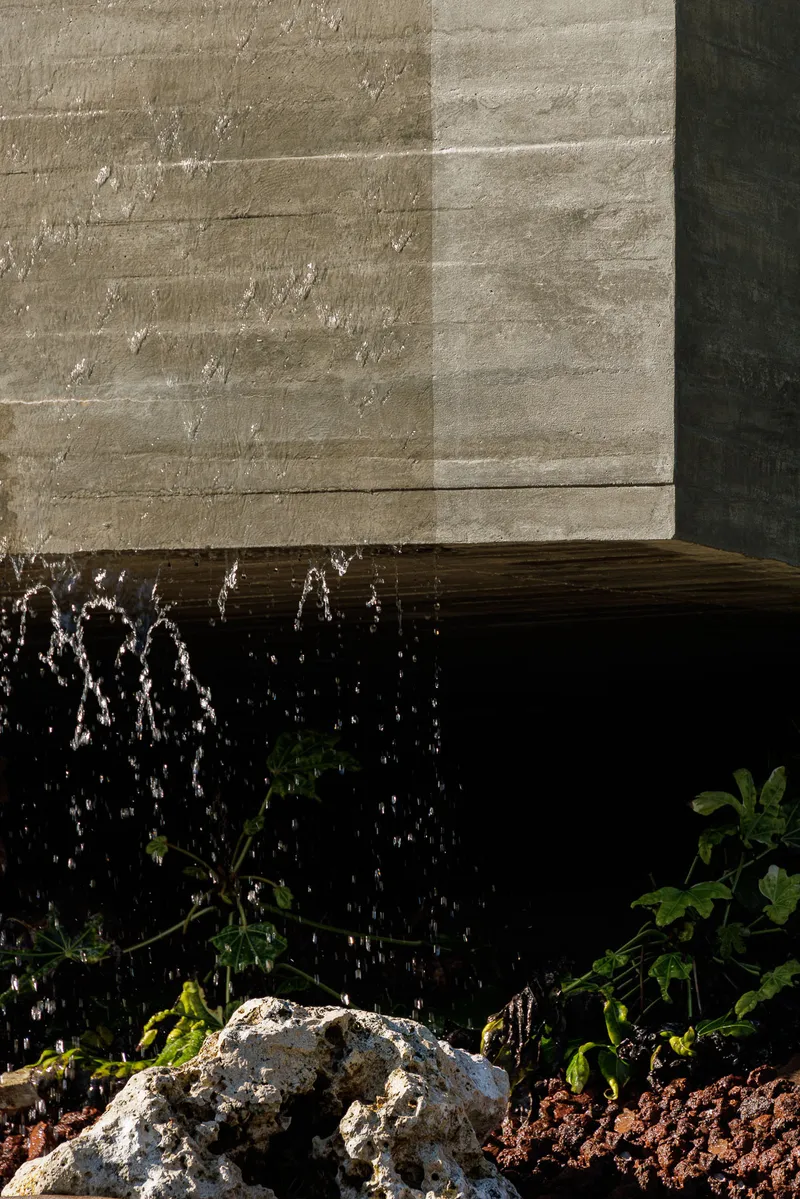 Water feature along a board-formed concrete wall with volcanic rock and planting bed below