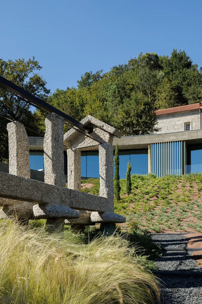 Granite water feature with carved channels beside gravel path and planted slope with grasses