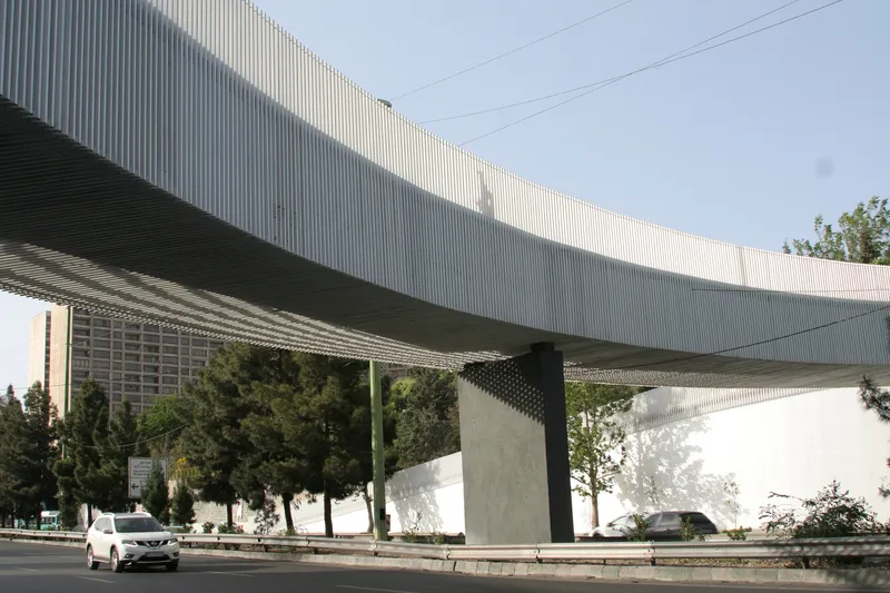 Underside of the bridge showing corrugated metal soffit and concrete support columns with passing vehicles below