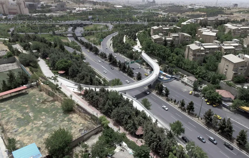 Aerial view of a curving pedestrian bridge crossing a multi-lane boulevard lined with trees