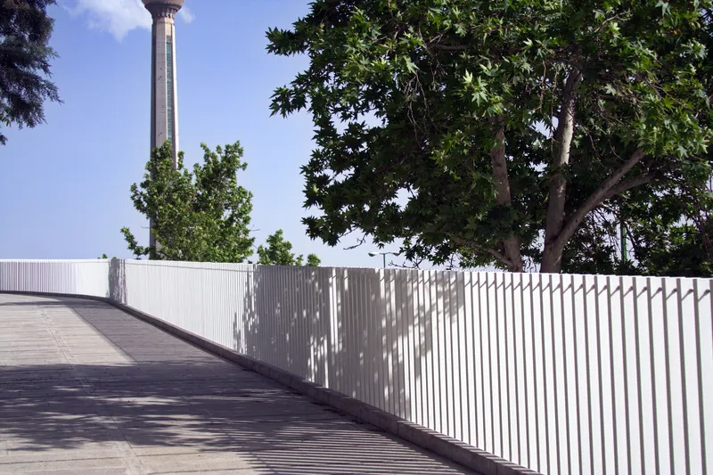White slatted balustrade curving through dappled tree shadows on the elevated walkway