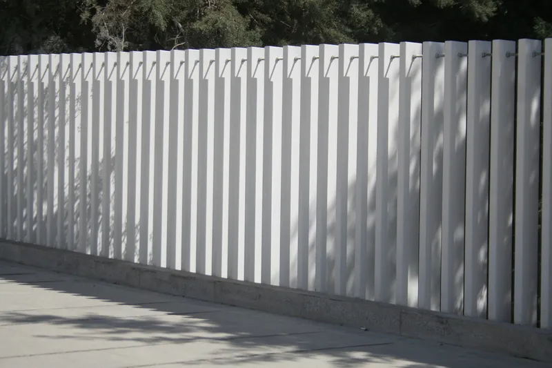 White vertical batten fence casting rhythmic shadows on a concrete base in bright sunlight