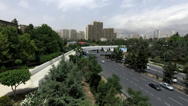 Elevated pedestrian walkway crossing above a multilane highway with apartment towers and mountains in the distance