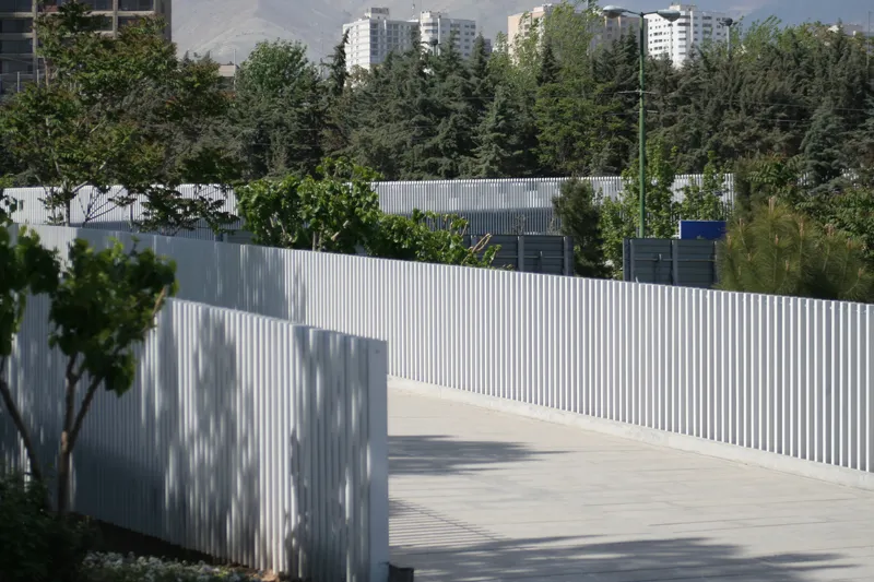 Pedestrian walkway bordered by white vertical slat railing with tree shadows cast on its surface