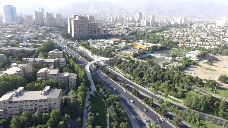 Aerial view of elevated pedestrian bridge arcing over a tree-lined highway through an urban district
