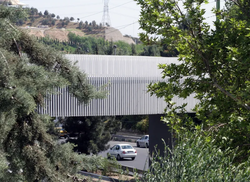 White vertical slat bridge span crossing above a roadway with hillside vegetation framing the view
