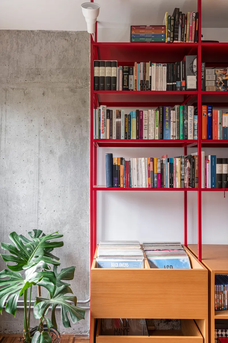 Red steel shelving against exposed concrete wall with timber drawer unit and potted plant