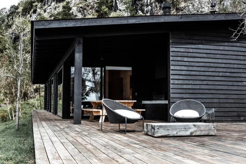 Covered deck with black steel columns and timber furniture beneath the deep eave and horizontal cladding