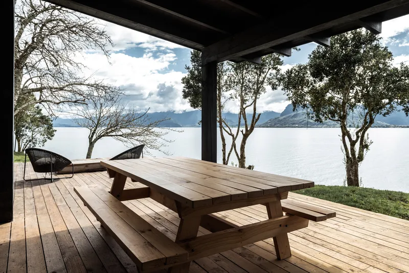 Timber picnic table under the porch roof framing views of the lake and scattered trees beyond